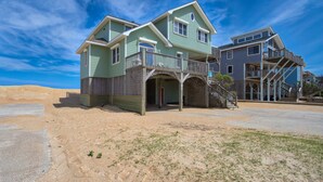 A beachfront house with a balcony, a covered porch, and a staircase leading to a second level. - The Sand Jewel: Oceanfront, Private Hot Tub, Pool Access (Avon)