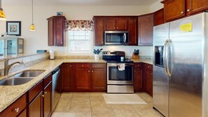 Una cocina con armarios de madera, electrodomésticos de acero inoxidable, encimera de granito y una ventana con un valance decorativo.