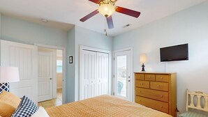 Un dormitorio con cama, cómoda, televisor y ventilador de techo.