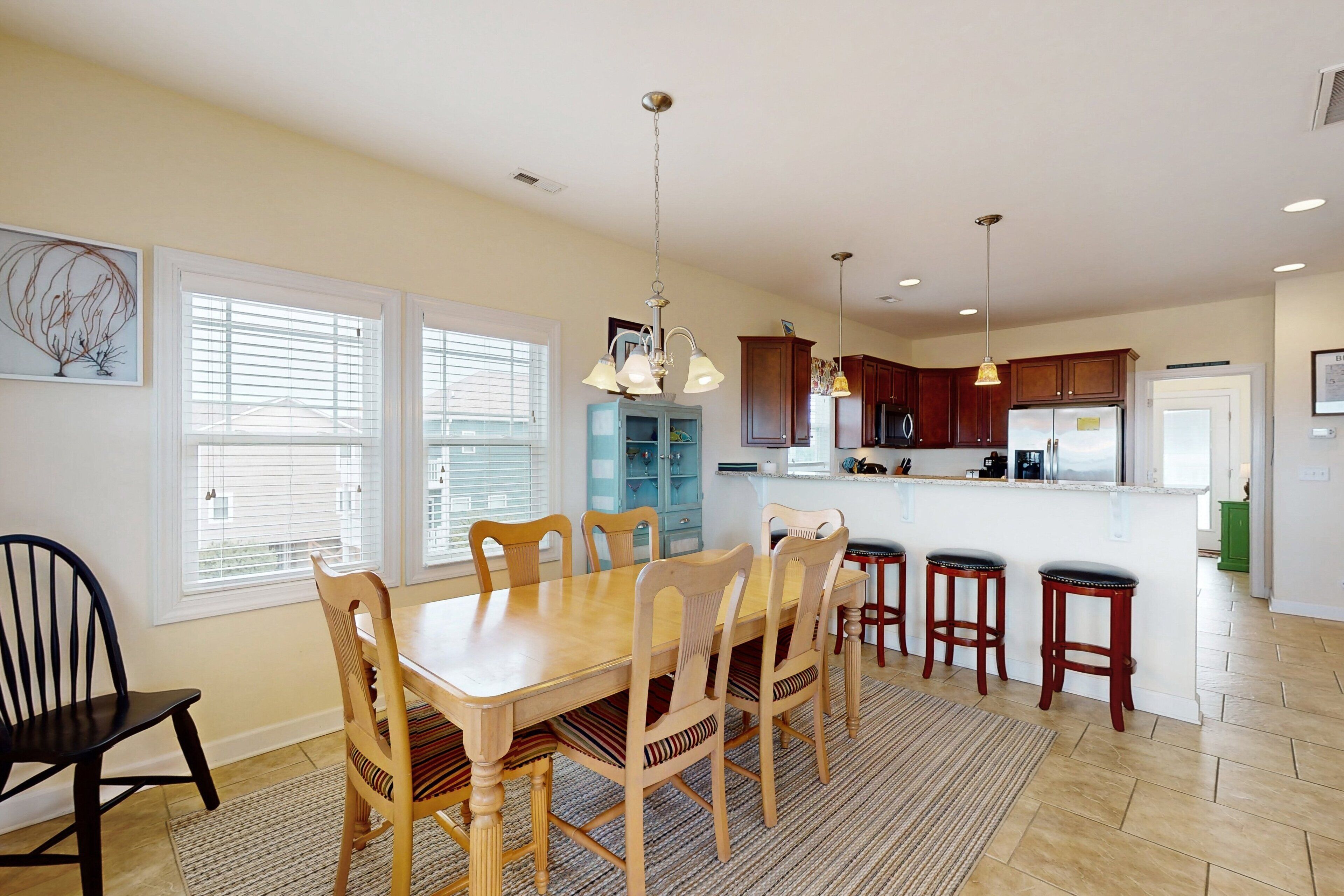 A dining area with a wooden table and chairs, a kitchen with wooden cabinets, and a window with blinds.