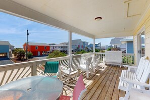 A covered porch with white chairs and a table, overlooking a residential area with houses and a street. - Coastal home close walk to the beach and local attractions (Surf City)