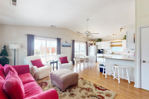 A spacious living area with a sofa, ottoman, and a dining table with chairs. A kitchen area is visible with a counter and stools. - Coastal home close walk to the beach and local attractions (Surf City)