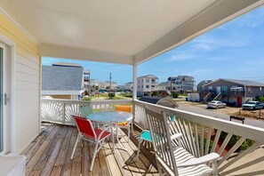 A covered porch with a table and chairs, overlooking a residential street with houses and parked cars. - Coastal home close walk to the beach and local attractions (Surf City)