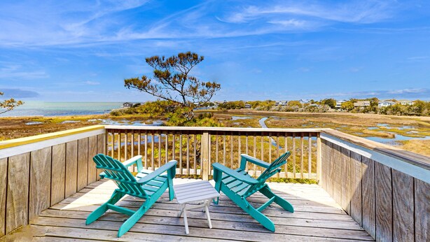 A wooden deck with two green Adirondack chairs and a small table, overlooking a coastal landscape with a tree and houses in the distance. - Dog-friendly House w/Water View, Free WiFi, AC, Private Hot Tub (Frisco)