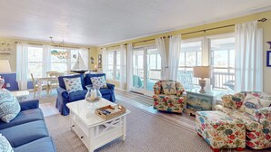 A spacious living room with a blue sofa, a white coffee table, and floral-patterned chairs. Large windows with curtains provide ample natural light. - Dog-friendly House w/Water View, Free WiFi, AC, Private Hot Tub (Frisco)