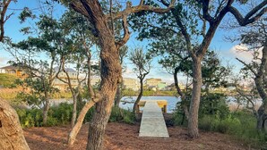 A wooden pathway leading to a dock over a body of water, surrounded by trees and buildings in the background.