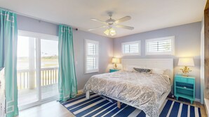 A bedroom with a bed, two bedside tables, a ceiling fan, and a view through a sliding glass door.