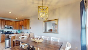 A modern kitchen with wooden cabinets, a stainless steel microwave, and a dining area with a wooden table and white chairs.