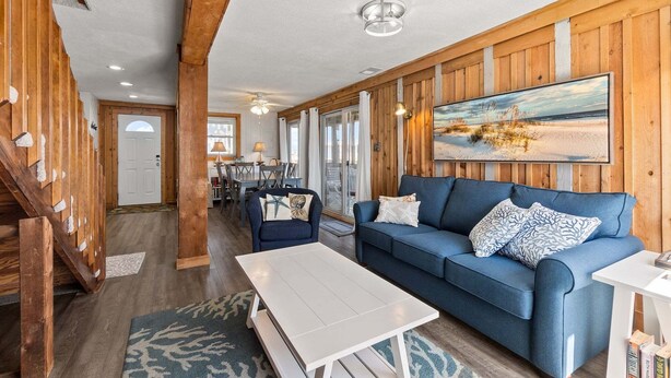 A spacious living area with a blue sofa, white coffee table, wooden walls, and a large painting of a beach scene.