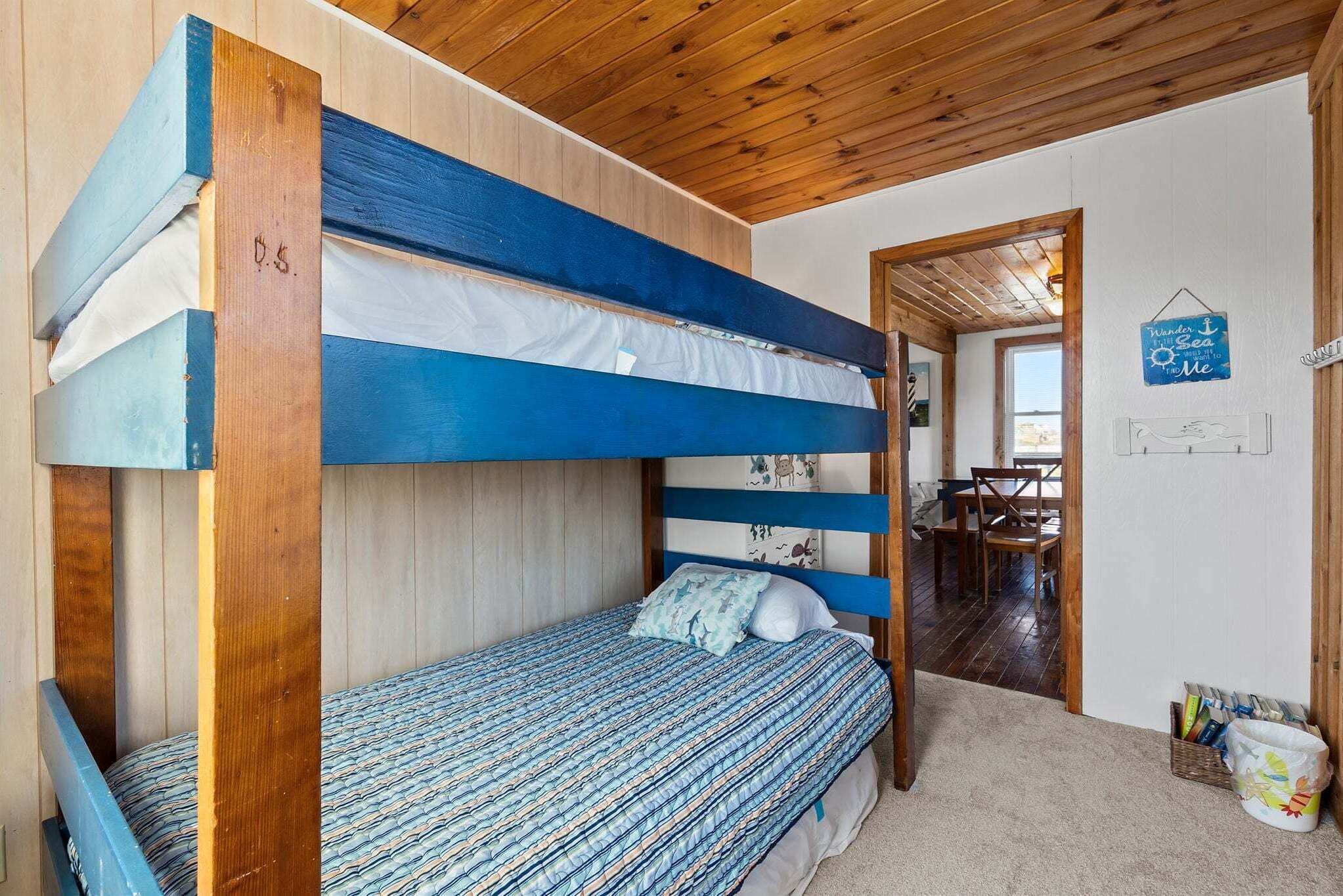 Un lit superposé avec une couvre-lit à motifs, un plafond en bois et une porte donnant sur un coin repas.