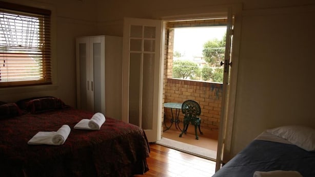 Quarto com duas camas, guarda-roupa e varanda com mesa e cadeira.