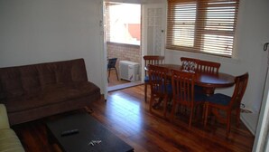 Uma sala de estar com um sofá marrom, uma mesa de centro preta e uma área de jantar com cadeiras e mesa de madeira.