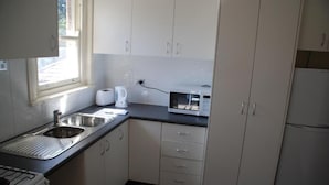 Uma cozinha compacta com armários brancos, uma pia de aço inoxidável, uma torradeira e um micro-ondas.
