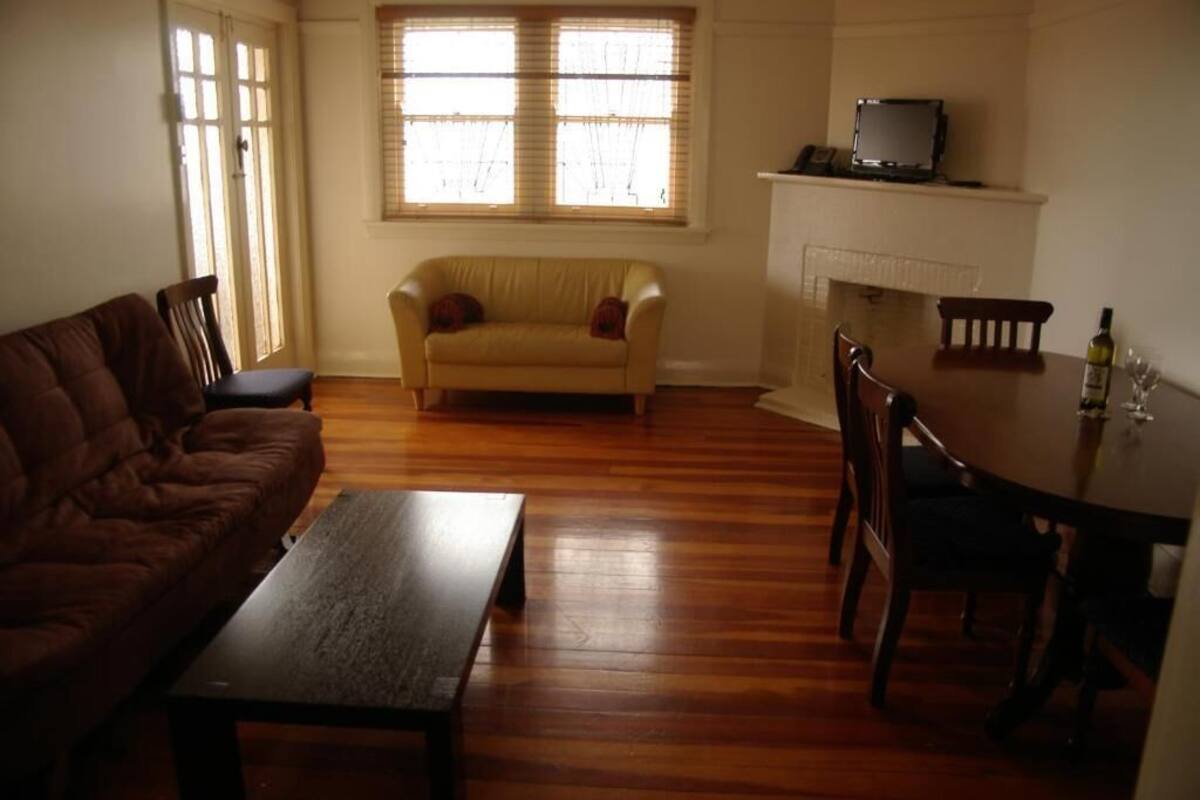 A living room with a brown sofa, a yellow armchair, a wooden coffee table, a dining table with chairs, and a fireplace.