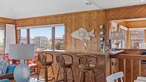 A wooden interior with a bar area, wicker chairs, a large fish decoration, and a view of buildings outside. - 4 bedroom house with ocean view, private hot tub & pool access (Avon)