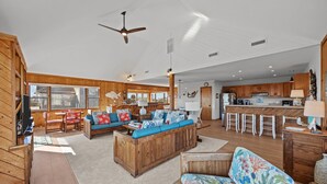 A spacious living area with wooden furniture, a kitchen, and large windows. - 4 bedroom house with ocean view, private hot tub & pool access (Avon)