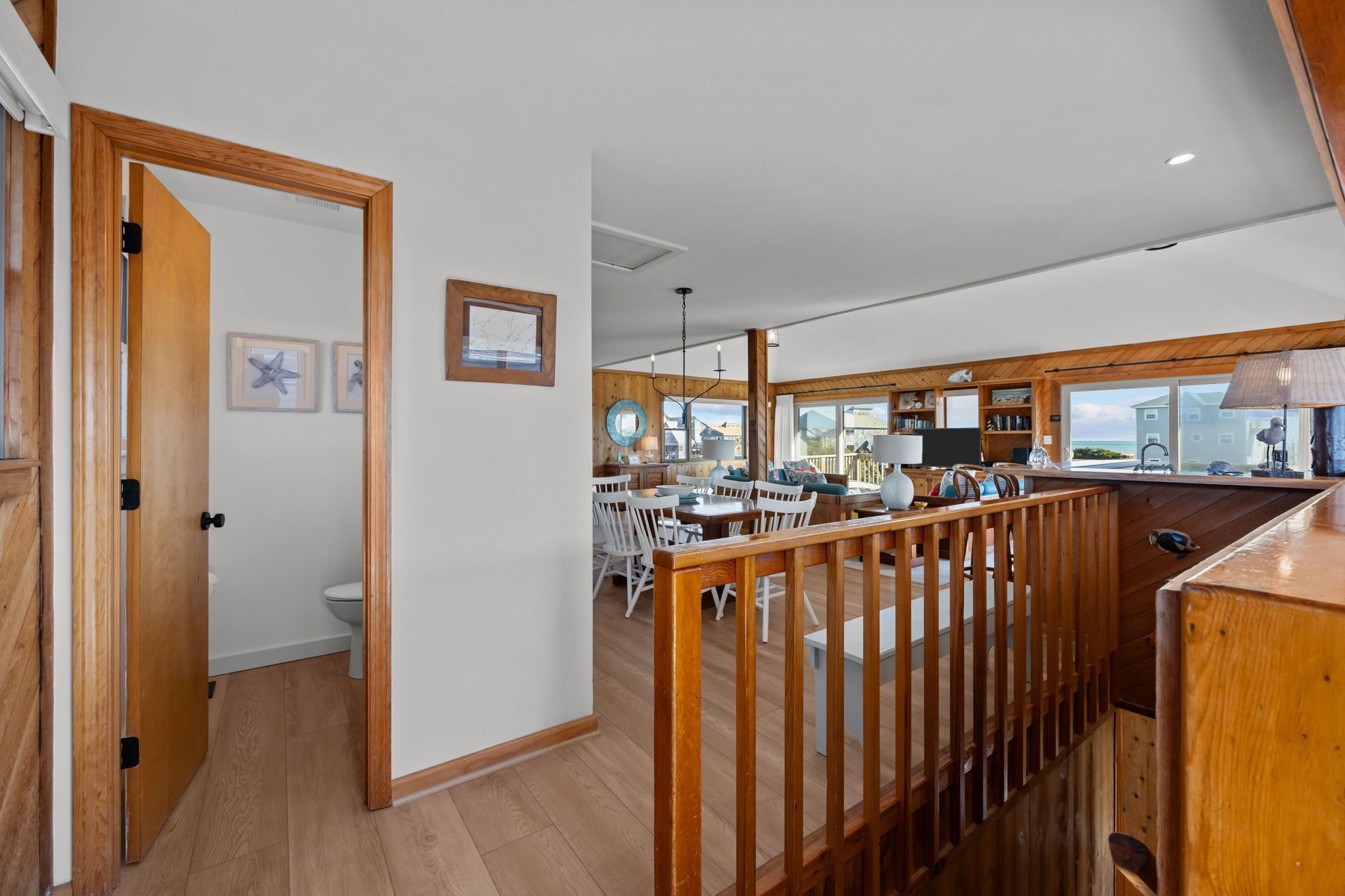 A spacious kitchen with wooden beams, a dining area with white chairs, and a view of the sea through large windows.