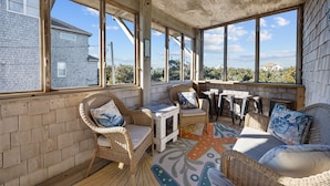 A sunlit room with wicker furniture, large windows, and a view of a house. - 4 bedroom house with ocean view, private hot tub & pool access (Avon)