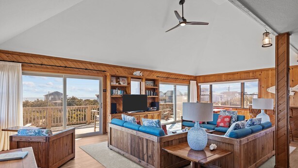 A spacious living room with a large wooden sofa, a coffee table, and a television. There is a balcony with a view of the city and a wooden deck. - 4 bedroom house with ocean view, private hot tub & pool access (Avon)