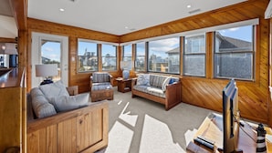 A spacious living area with wooden walls and large windows, furnished with sofas and a coffee table. - 4 bedroom house with ocean view, private hot tub & pool access (Avon)