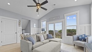 A spacious living room with a grey sectional sofa, a ceiling fan, and large windows offering a view of the outdoors. - Stunning sound view home, close to the beach in the heart of Surf City (Surf City)