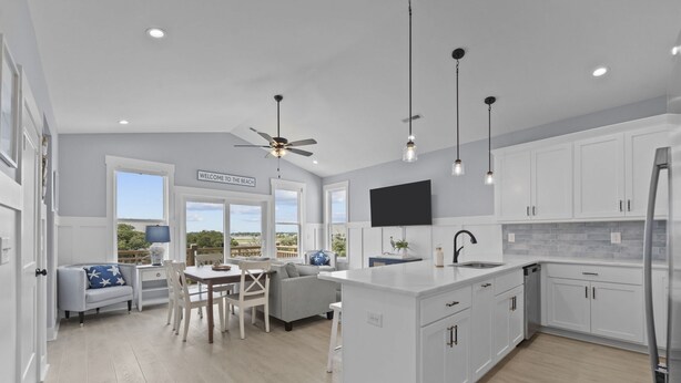 A modern kitchen with white cabinetry, a central island, and a dining area with a gray sofa and table. - Stunning sound view home, close to the beach in the heart of Surf City (Surf City)
