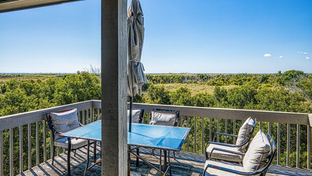 A covered outdoor seating area with a table and chairs, overlooking a natural landscape. - Ocean and waterway-view duplex - pool, beach access, washer/dryer, central AC (Topsail Beach)