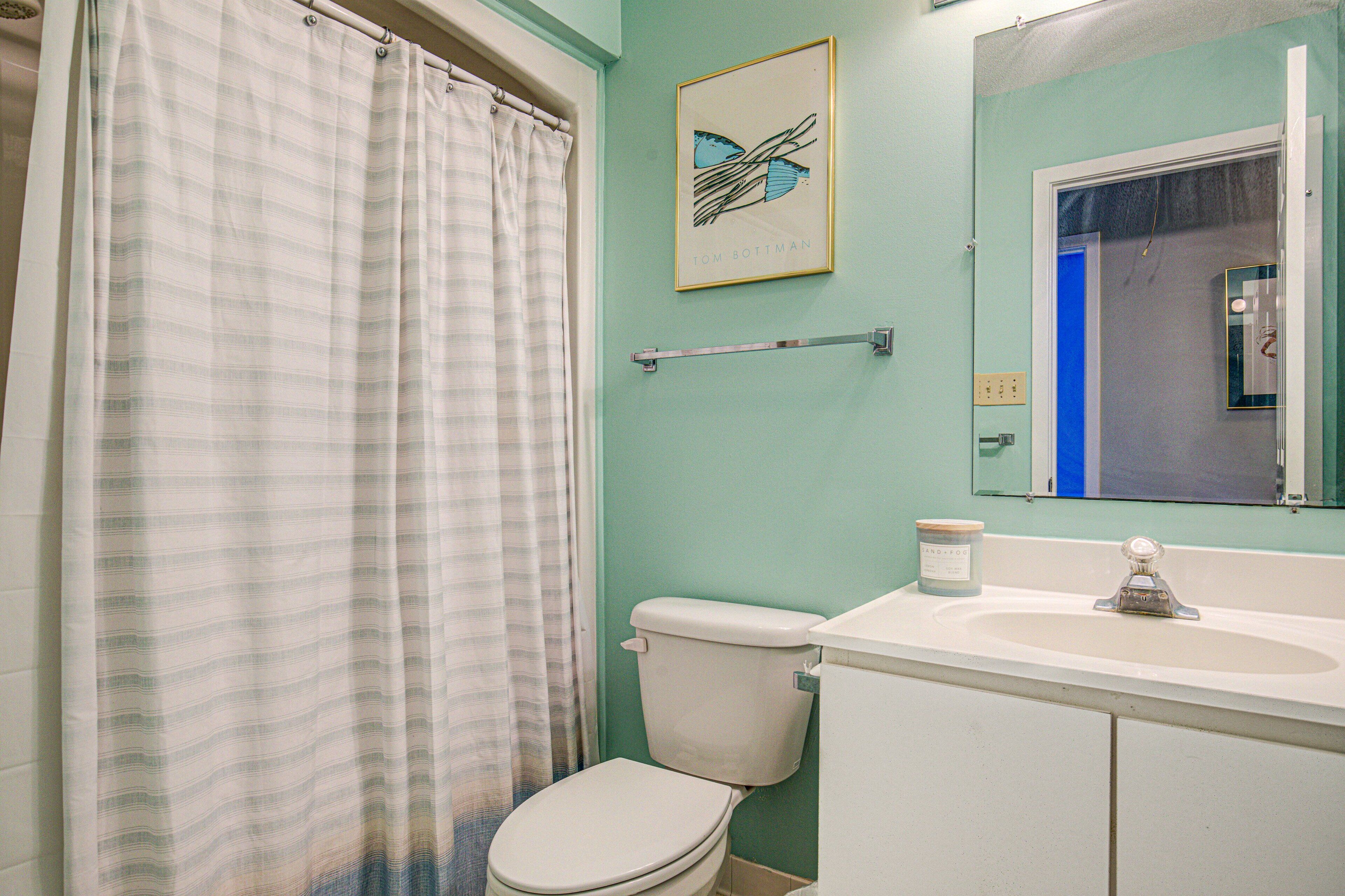 A bathroom with a striped shower curtain, a toilet, a sink with a mirror, and a framed picture on the wall.