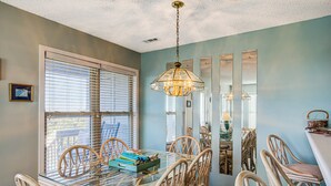 A dining area with a glass table, wicker chairs, and a hanging light fixture. - Ocean and waterway-view duplex - pool, beach access, washer/dryer, central AC (Topsail Beach)