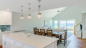 A spacious kitchen with a large island, wooden chairs, and pendant lighting. - Oceanfront home with beach access, a game room, washer/dryer, & central AC (Topsail Beach)