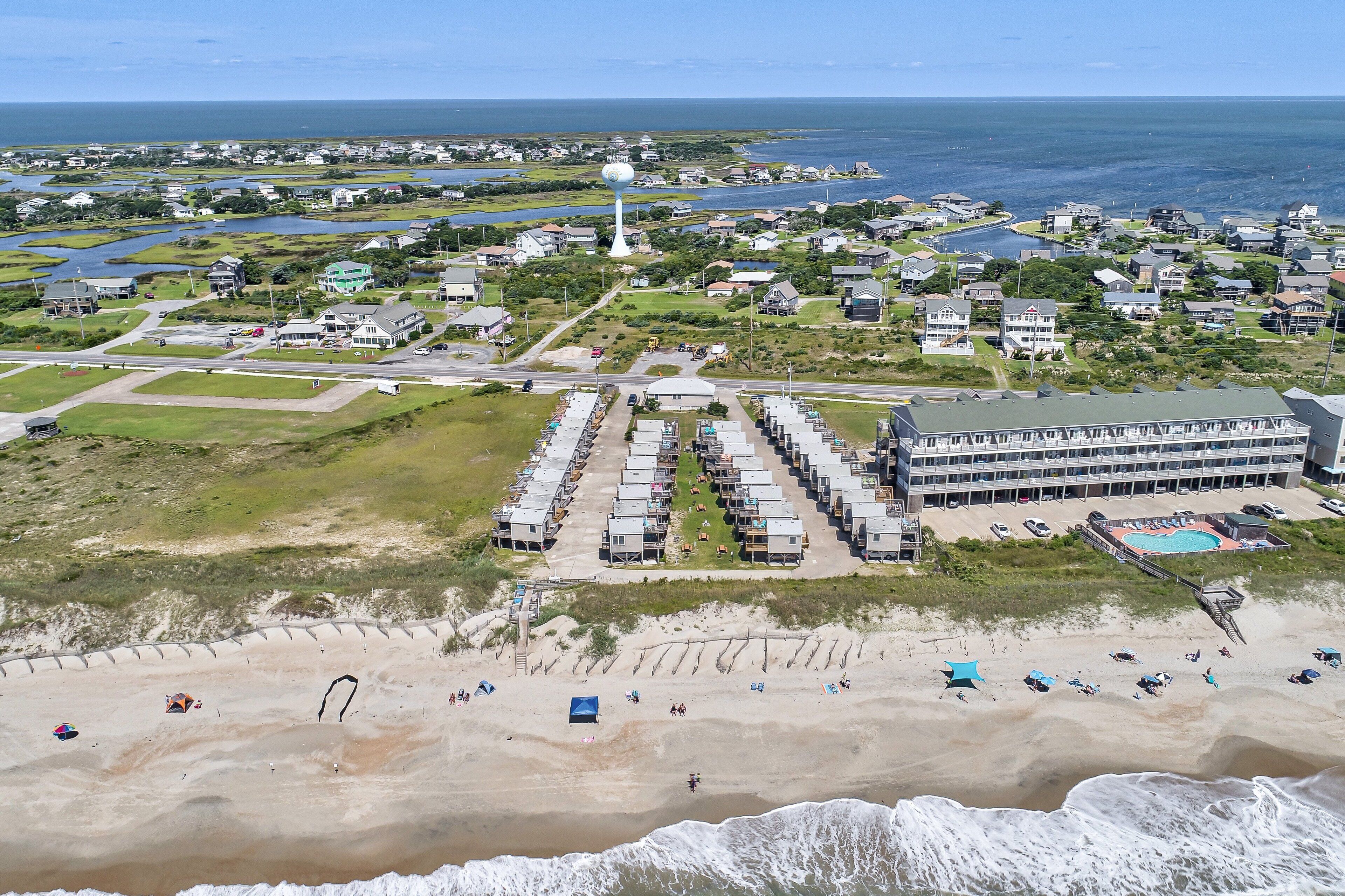 Une vue aérienne d’une ville côtière, avec une plage, un grand immeuble à plusieurs étages et un château d’eau.