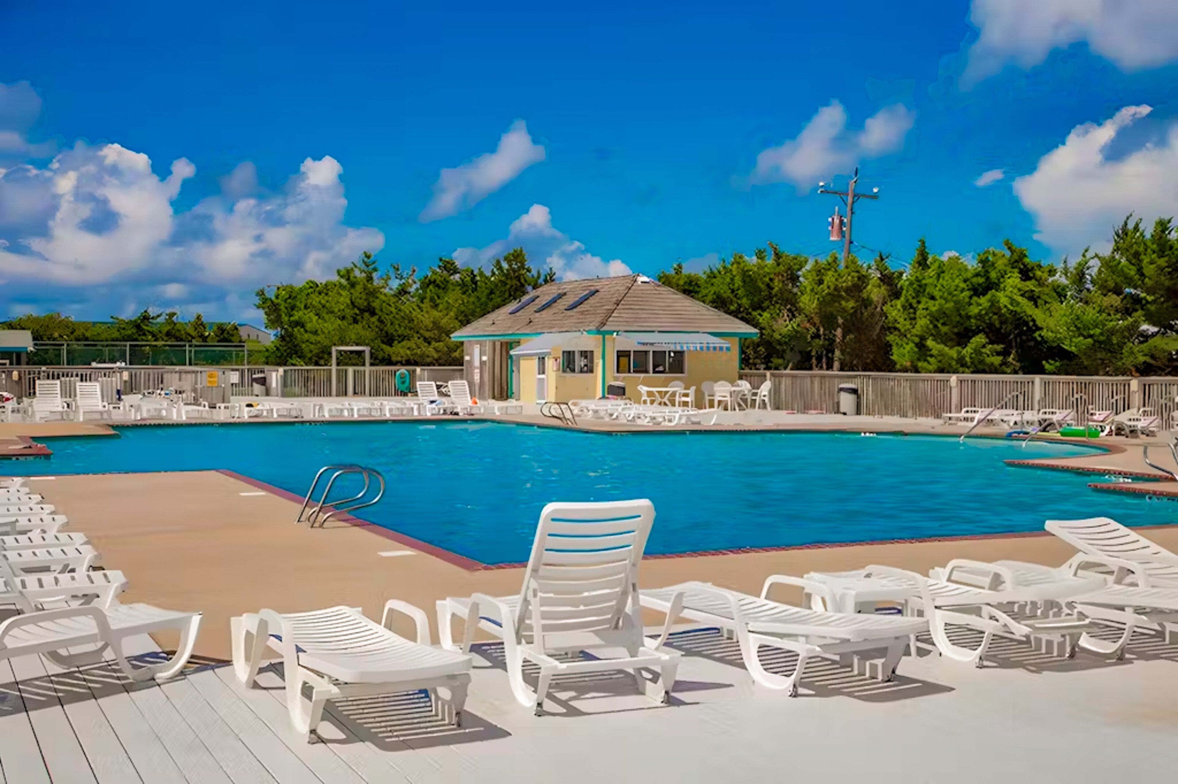 A swimming pool with lounge chairs, a small building, and a fenced area.