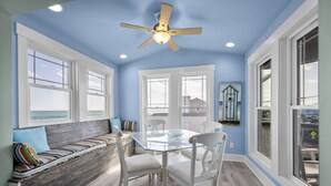 A dining area with a glass table, white chairs, and a ceiling fan. - Beachfront home with stunning views, elevator and multiple decks (Topsail Beach)