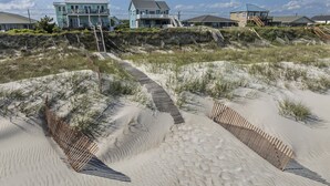 A beachfront property with a sandy pathway leading to a house with a balcony. - Beachfront home with stunning views, elevator and multiple decks (Topsail Beach)
