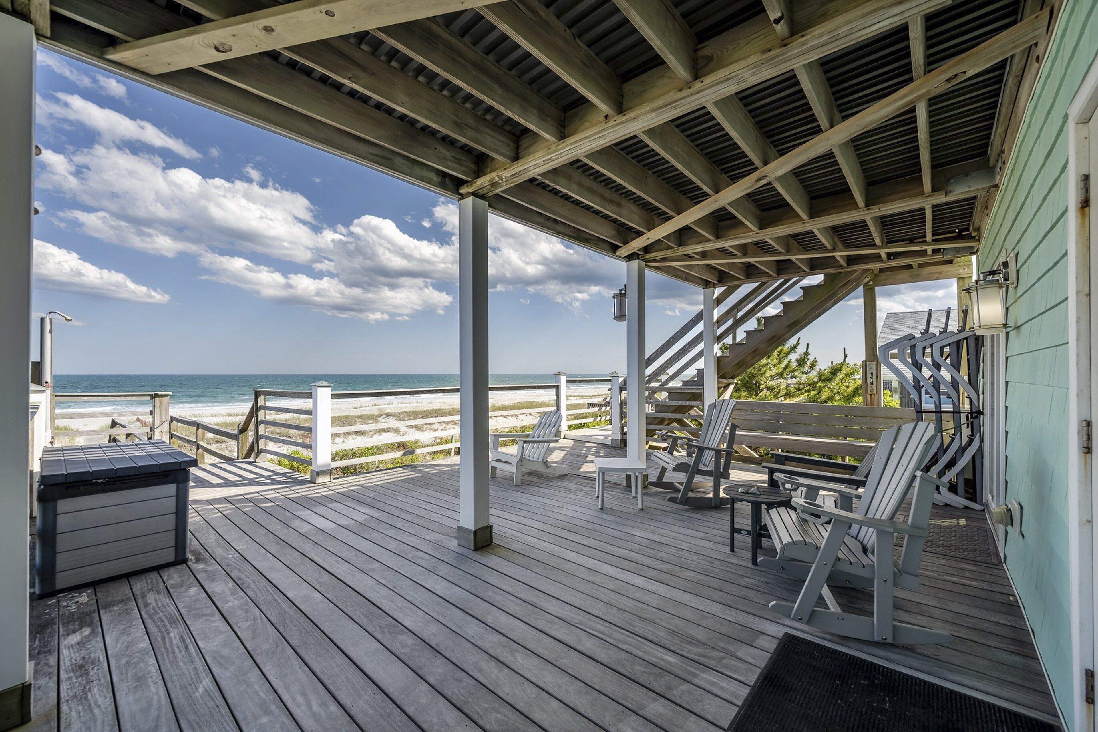 Eine Holzterrasse mit Sitzgelegenheiten mit Blick auf einen Strand.