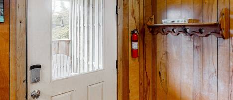 A wooden door with a window, a fire extinguisher mounted on the wall, and a small shelf above the door.