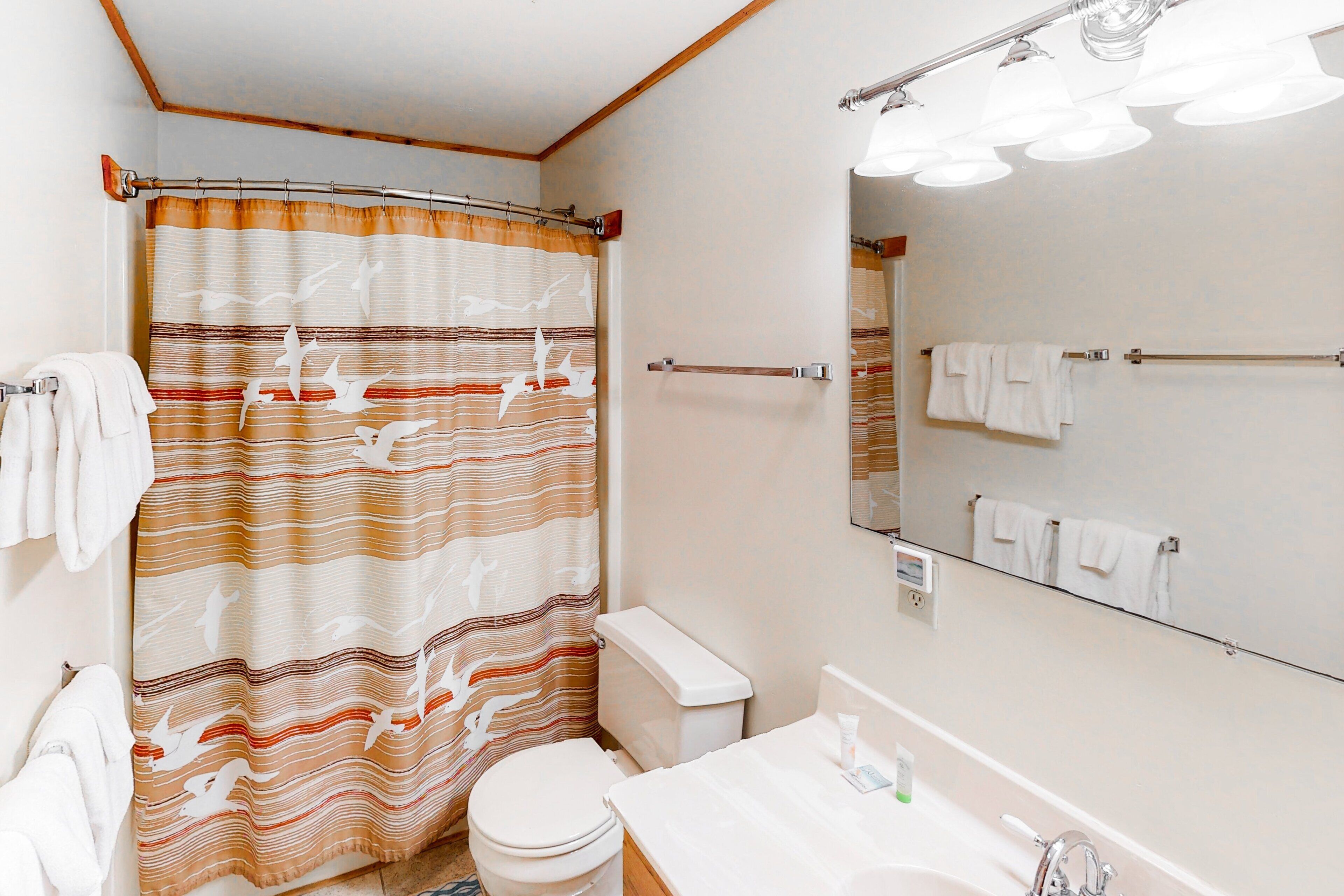 Een badkamer met een gestreept douchegordijn, een toilet, een wastafel met spiegel en meerdere handdoeken op rekken.