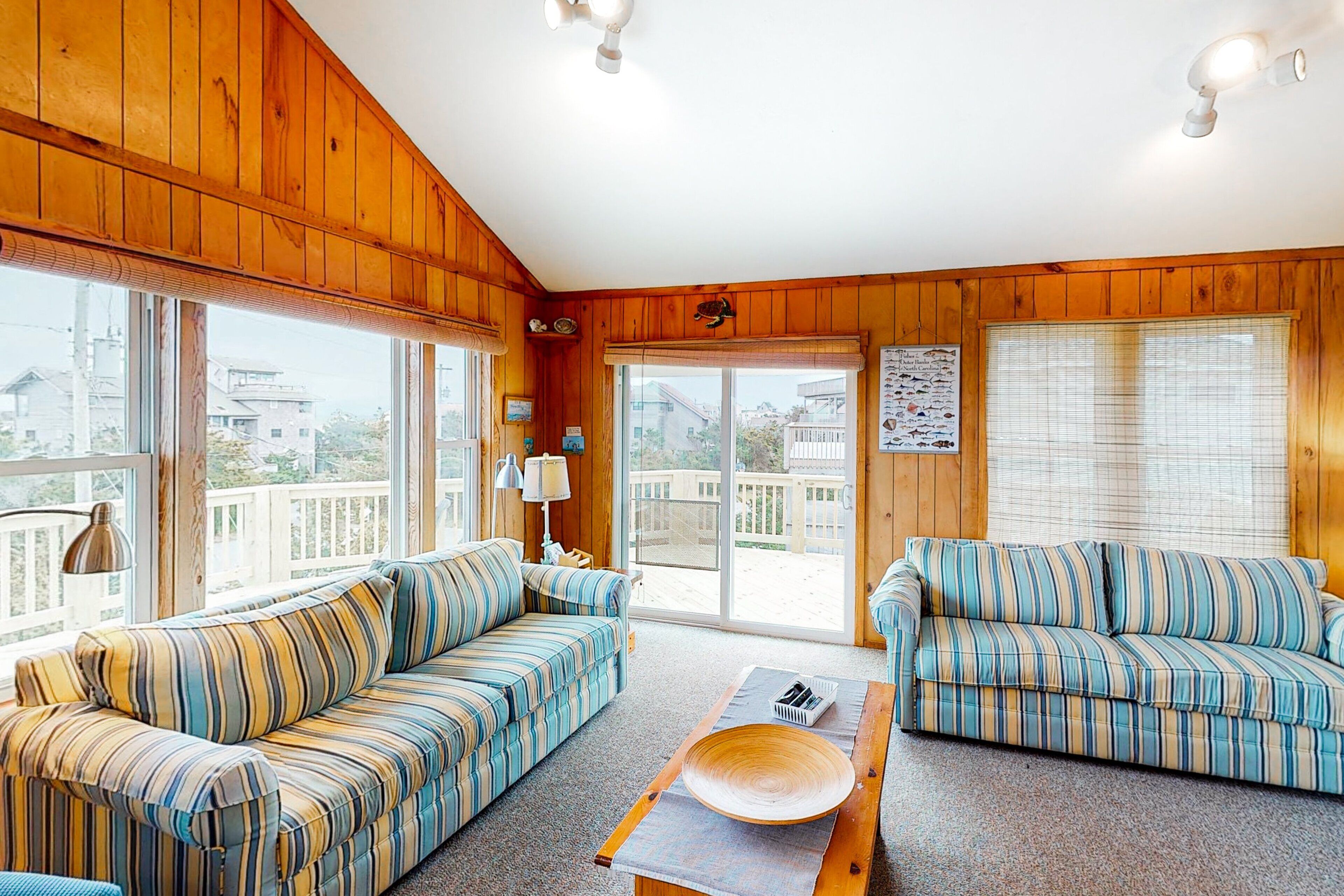 A cozy room with wooden walls and large windows, featuring two striped sofas and a wooden coffee table.
