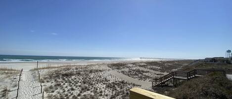 A beach with a wooden walkway leading to a pier.