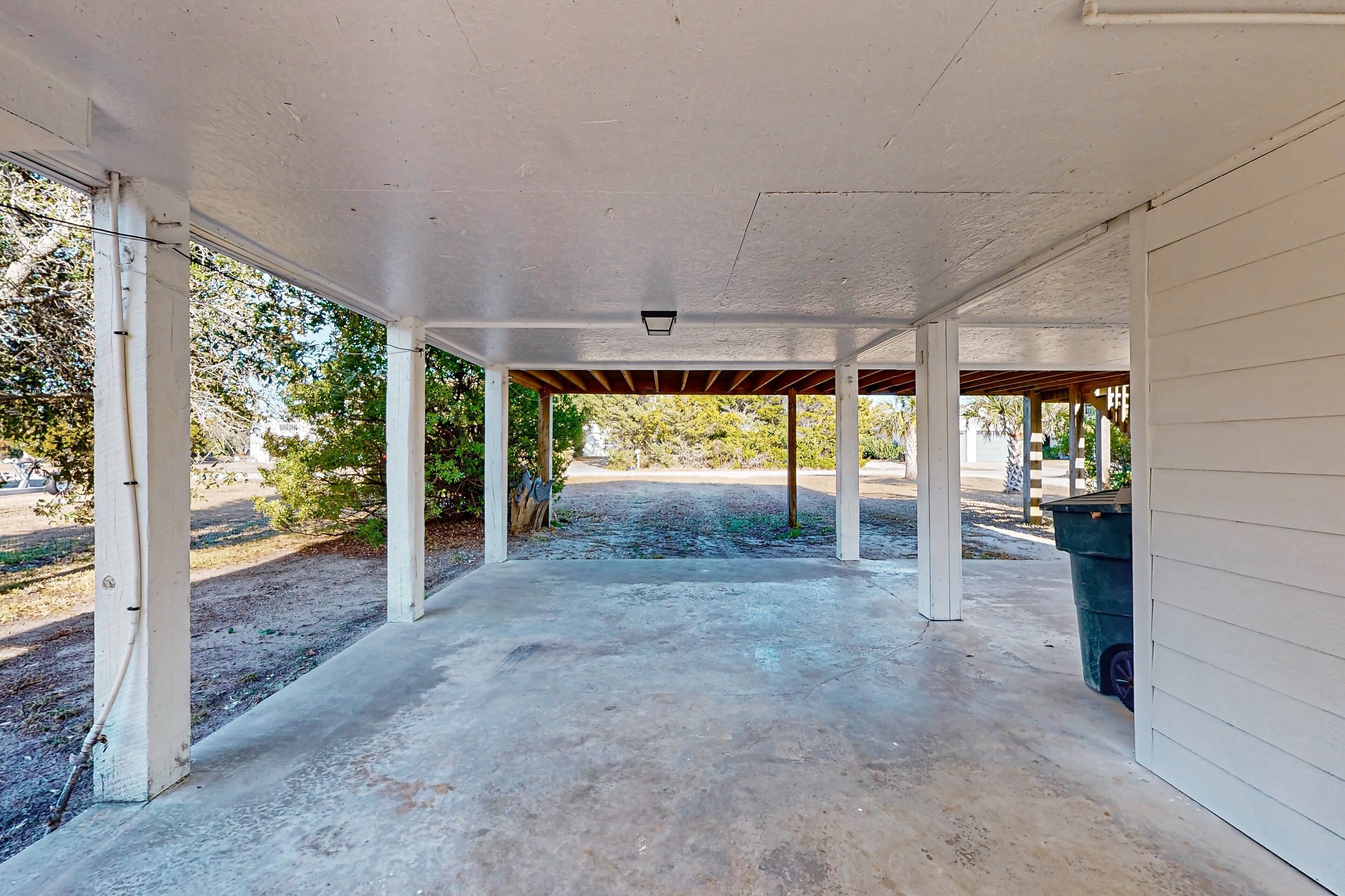 An empty covered patio with concrete flooring and white pillars.