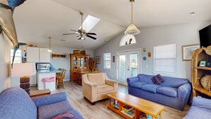 A spacious living room with a sofa, armchair, and coffee table. There is a dining area with a table and chairs, and a kitchen in the background. - Coastal home with large deck, close to beach and local attractions (Topsail Beach)