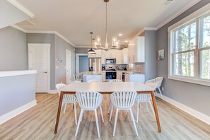A modern kitchen with white cabinetry, a central island, and a dining area with white chairs. - COASTAL DUPLEX 🌊 | WALK TO BEACH | FAMILY & DOG-FRIENDLY 🐾 (Carolina Beach)