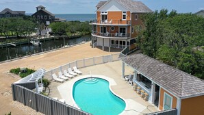 A two-story building with a pool and outdoor seating area, overlooking a body of water. - Waterfront home with ocean views, private pool, hot tub, & Tesla/EV charger (Frisco)