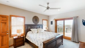 A bedroom with a bed, wooden nightstands, a ceiling fan, and a view through a large window. - Waterfront home with ocean views, private pool, hot tub, & Tesla/EV charger (Frisco)