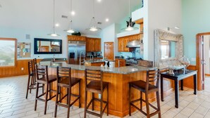 A spacious kitchen with a large island, wooden bar stools, and pendant lighting. - Waterfront home with ocean views, private pool, hot tub, & Tesla/EV charger (Frisco)