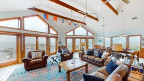 A spacious living room with large windows, a high ceiling, and a cozy seating area. - Waterfront home with ocean views, private pool, hot tub, & Tesla/EV charger (Frisco)