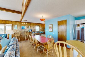 Une pièce chaleureuse avec une table à manger en bois, des chaises, un canapé et un coin cuisine équipé d’un réfrigérateur.
