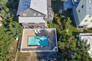 Vue aérienne d’un quartier résidentiel avec une piscine entourée d’une clôture blanche, des maisons voisines et une végétation luxuriante.