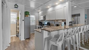 Una cucina moderna con mobili bianchi, ripiani in granito e un'isola centrale con sgabelli da bar.