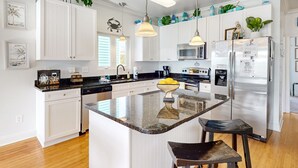 A modern kitchen with white cabinets, a central island, stainless steel appliances, and pendant lighting.